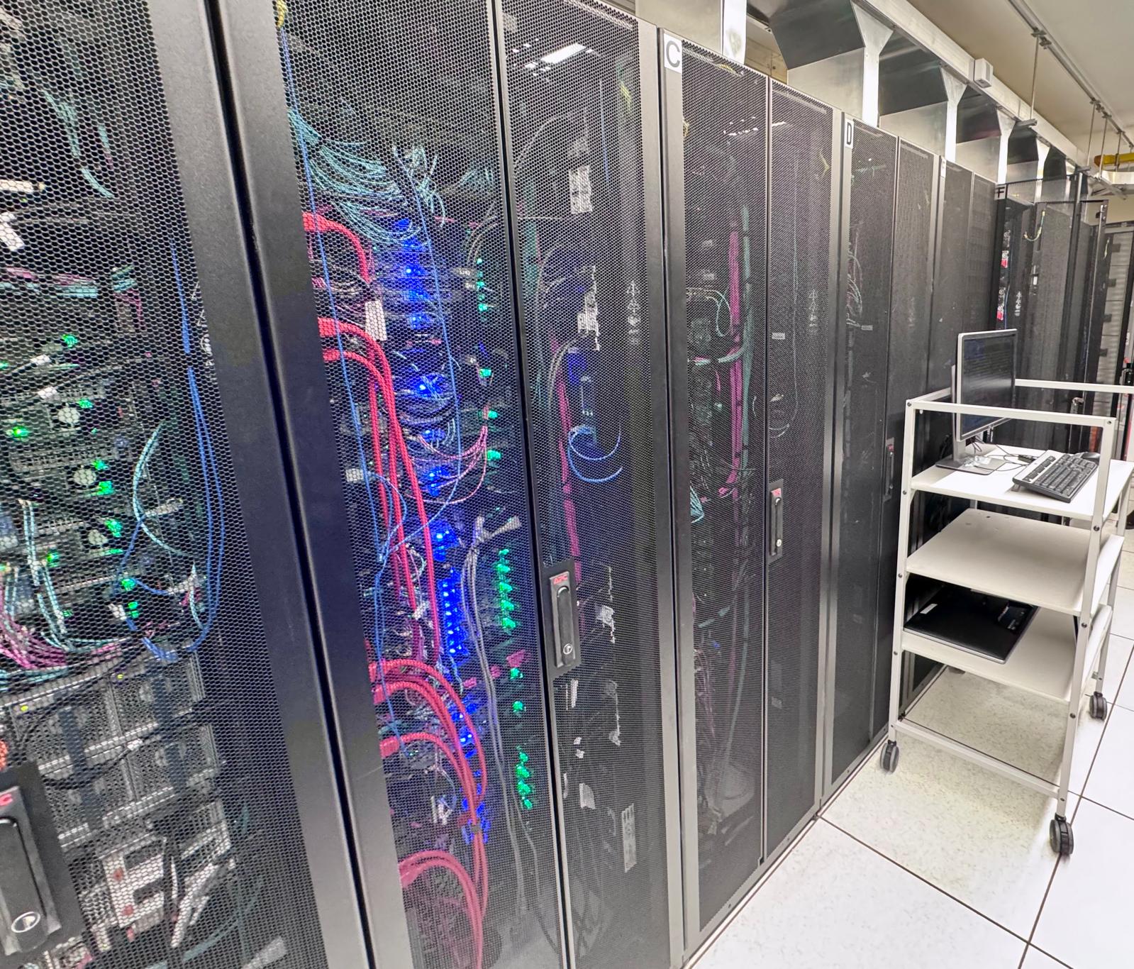 The rear of the same row of cabinets, showing bundled network and power cabling and rows of status lights.